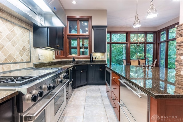 kitchen with decorative backsplash, appliances with stainless steel finishes, dark stone counters, light tile patterned floors, and hanging light fixtures