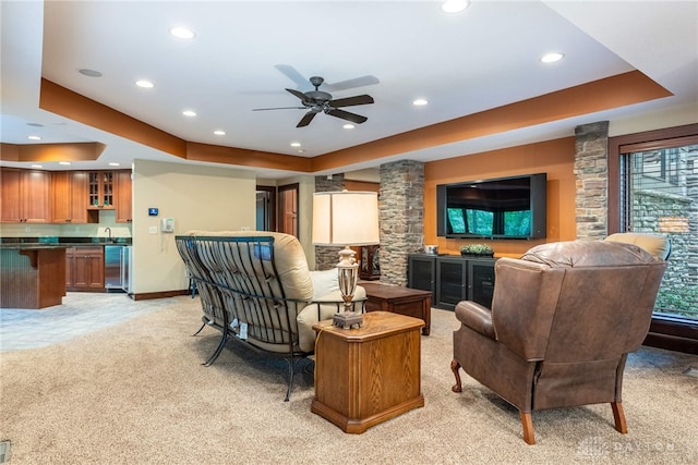 carpeted living room with ceiling fan, a raised ceiling, and decorative columns