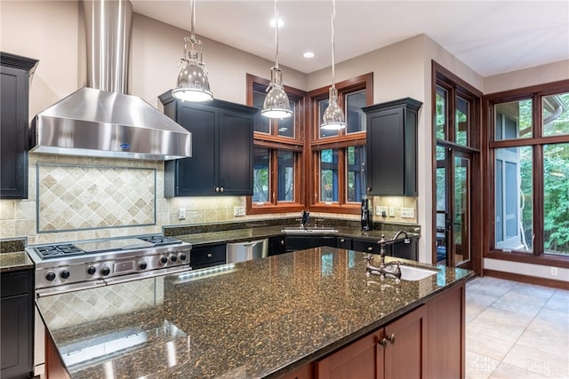 kitchen featuring sink, hanging light fixtures, dark stone counters, and wall chimney range hood