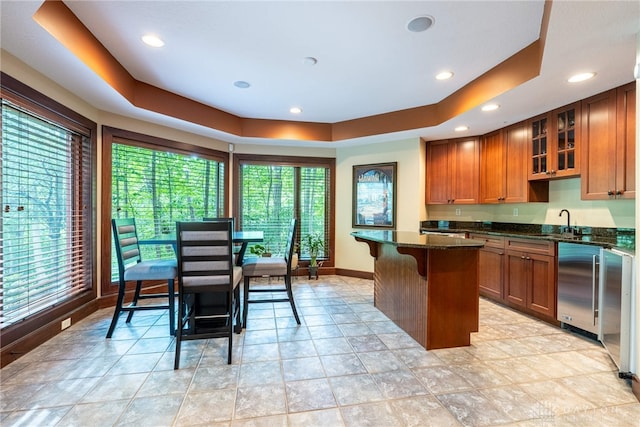 kitchen with a raised ceiling, a kitchen island, dark stone counters, and a breakfast bar area