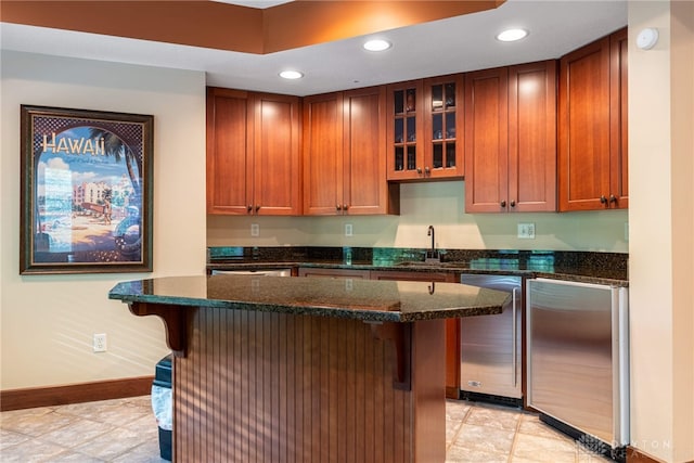 kitchen with a kitchen bar, dishwasher, dark stone counters, and fridge