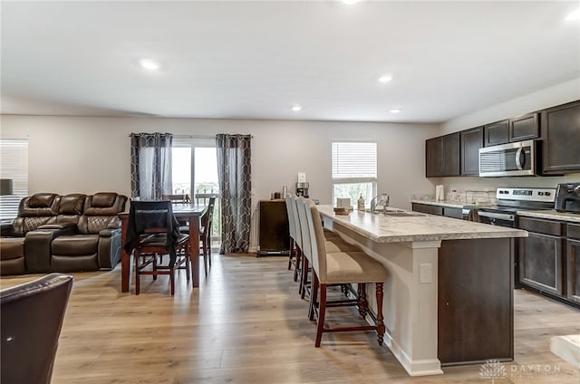 kitchen featuring stainless steel appliances, a wealth of natural light, a center island with sink, and a breakfast bar