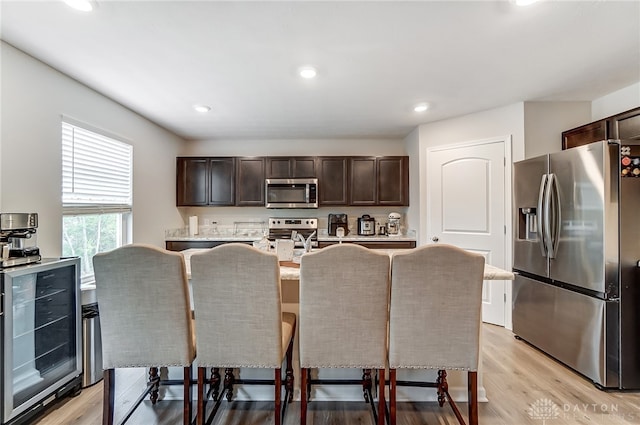 kitchen with stainless steel appliances, dark brown cabinetry, wine cooler, a breakfast bar, and light hardwood / wood-style flooring