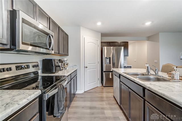 kitchen featuring light stone counters, light wood-type flooring, appliances with stainless steel finishes, dark brown cabinets, and sink