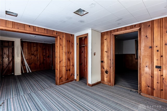 basement with ornamental molding, wood walls, and dark colored carpet