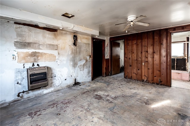 unfurnished living room with ceiling fan, heating unit, and wooden walls