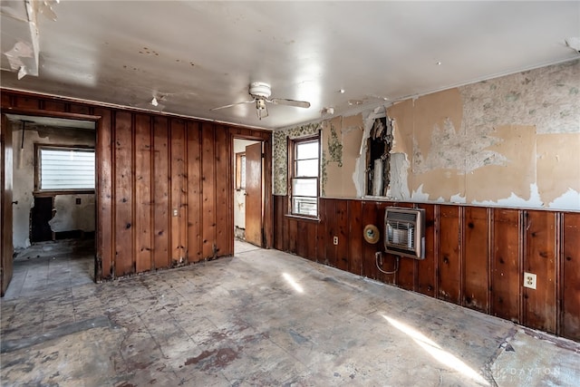 spare room featuring heating unit, wooden walls, ceiling fan, and a wood stove