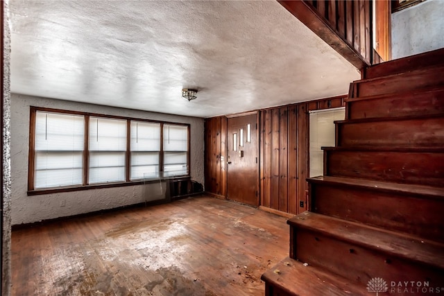 staircase with a textured ceiling, wooden walls, and hardwood / wood-style floors