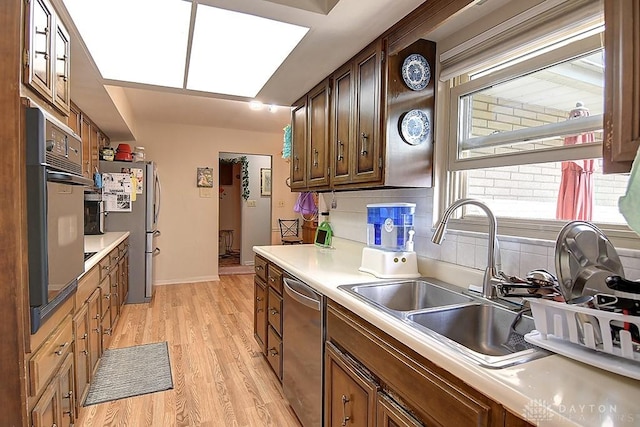 kitchen featuring stainless steel appliances, light countertops, backsplash, a sink, and light wood-type flooring