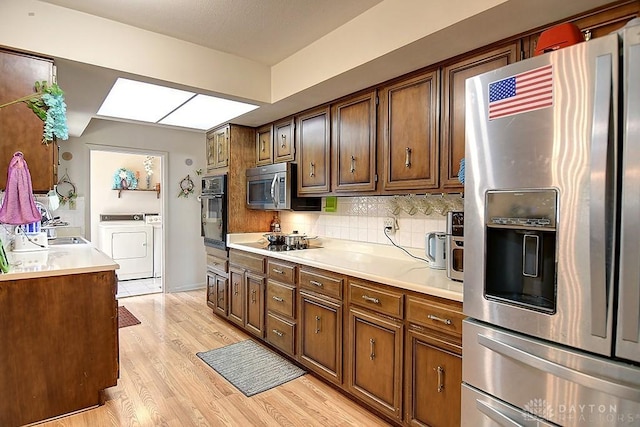 kitchen featuring light wood-style floors, light countertops, backsplash, black appliances, and washer and clothes dryer