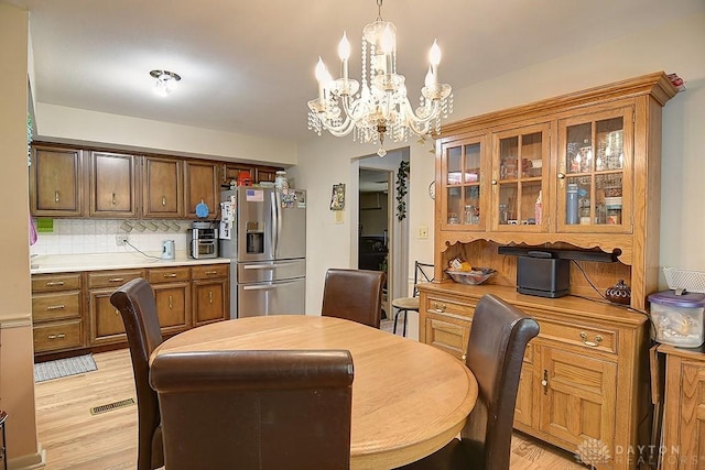 dining space with light wood finished floors, visible vents, and an inviting chandelier