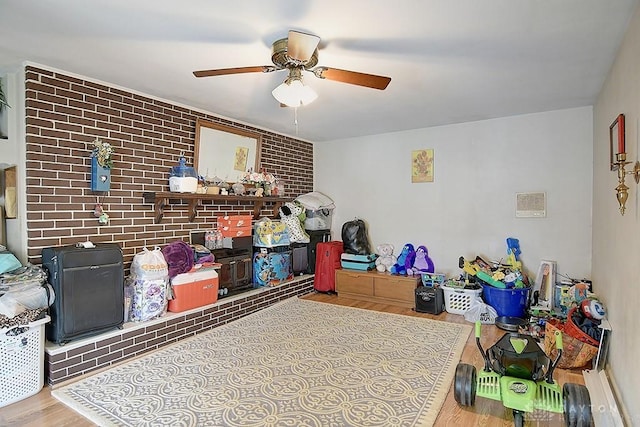 game room featuring brick wall, wood finished floors, and a ceiling fan