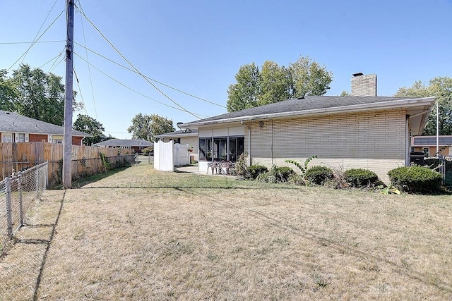 back of house with brick siding, fence, a chimney, and a lawn