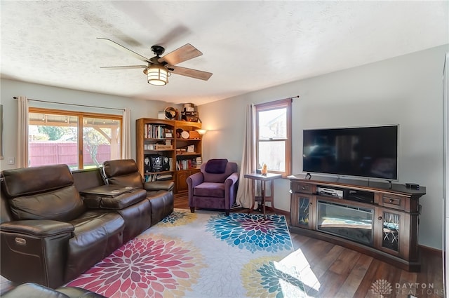 living room featuring ceiling fan, dark wood-type flooring, a healthy amount of sunlight, and a textured ceiling