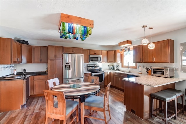 kitchen featuring pendant lighting, wood-type flooring, sink, appliances with stainless steel finishes, and kitchen peninsula