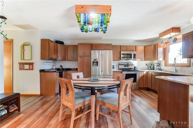 kitchen featuring light stone countertops, appliances with stainless steel finishes, backsplash, sink, and light hardwood / wood-style flooring