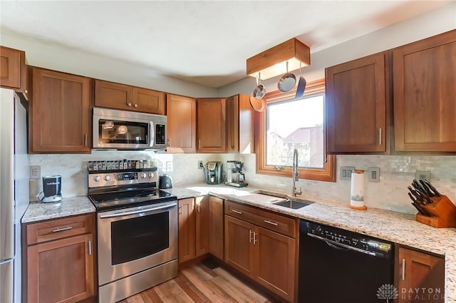 kitchen with sink, stainless steel appliances, tasteful backsplash, light stone counters, and light hardwood / wood-style flooring