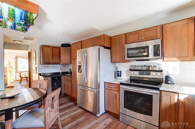 kitchen with light stone countertops, appliances with stainless steel finishes, decorative backsplash, beverage cooler, and wood-type flooring