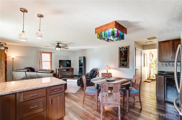 kitchen with ceiling fan, light stone countertops, light wood-type flooring, a textured ceiling, and decorative light fixtures