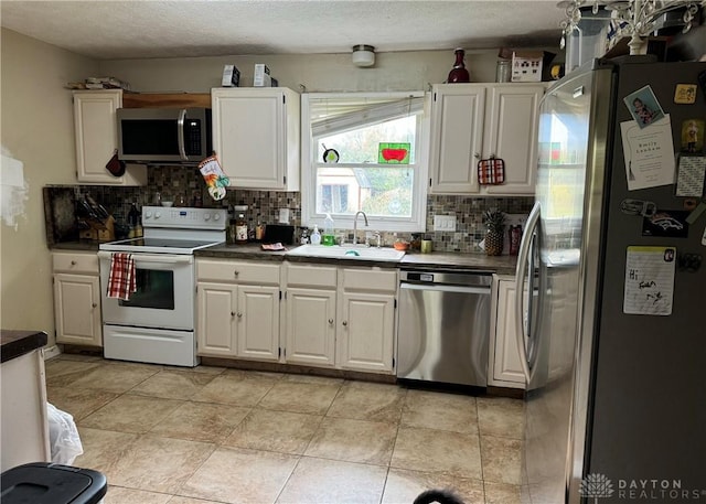 kitchen featuring stainless steel appliances, dark countertops, tasteful backsplash, white cabinetry, and a sink