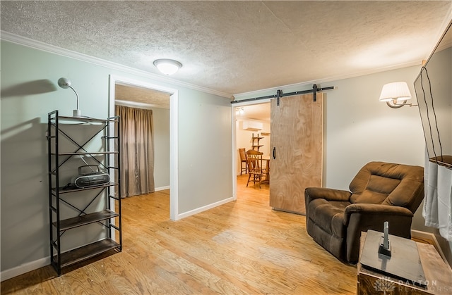 living area with a wall mounted AC, a textured ceiling, a barn door, light hardwood / wood-style flooring, and ornamental molding