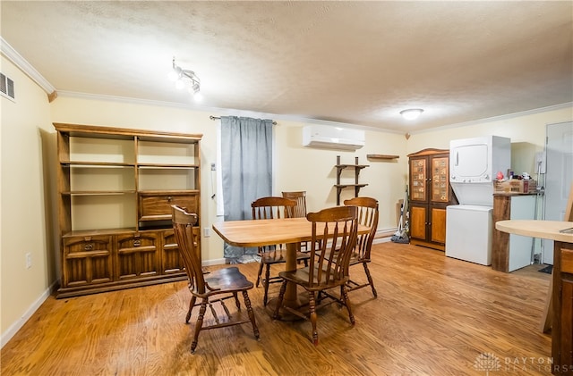 dining space featuring crown molding, a textured ceiling, light hardwood / wood-style floors, stacked washer / drying machine, and a wall mounted AC