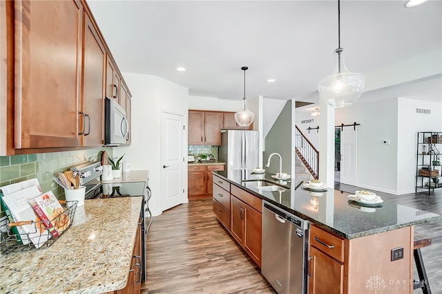 kitchen featuring hardwood / wood-style floors, a barn door, stainless steel appliances, and a kitchen island with sink