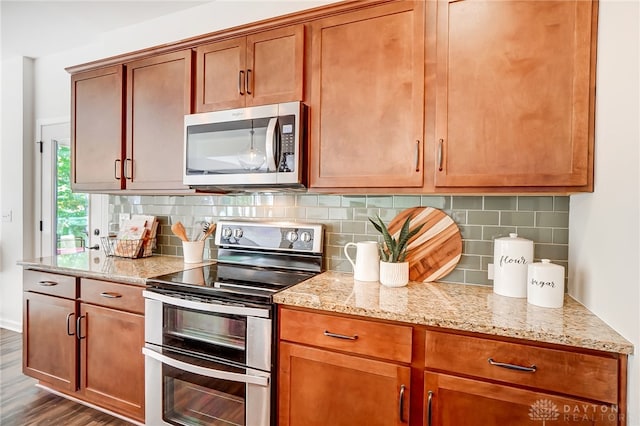 kitchen featuring light stone countertops, dark hardwood / wood-style flooring, stainless steel appliances, and backsplash