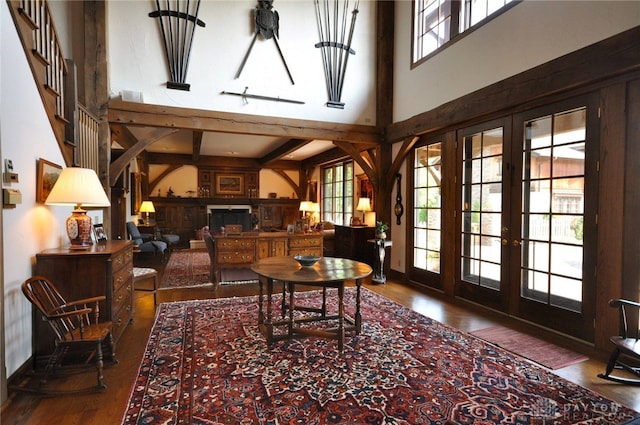 living area featuring beam ceiling, wood-type flooring, a towering ceiling, and french doors