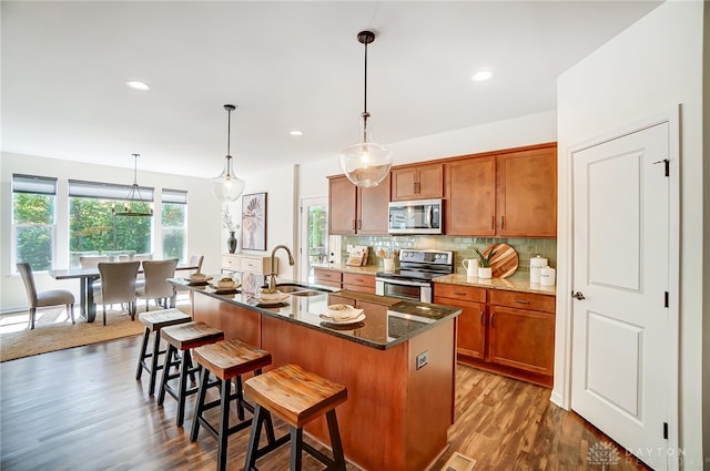 kitchen featuring sink, dark wood-type flooring, stainless steel appliances, a breakfast bar area, and a center island with sink