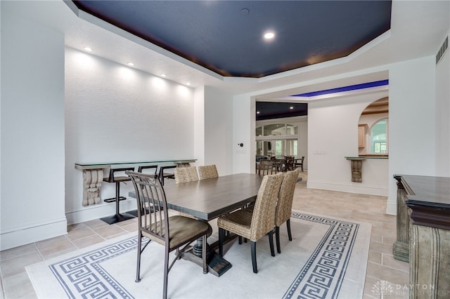 dining space with a tray ceiling and light tile patterned floors