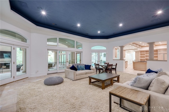 living room featuring a healthy amount of sunlight, a raised ceiling, french doors, and ornate columns