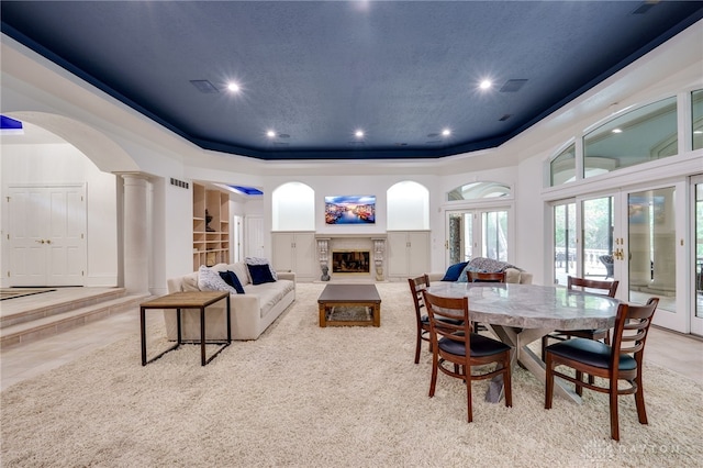 carpeted dining area featuring french doors, a tray ceiling, a fireplace, and ornate columns