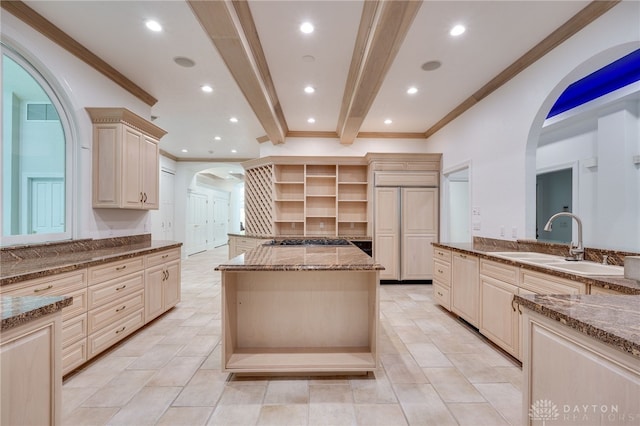 kitchen with light stone counters, beamed ceiling, sink, and a kitchen island