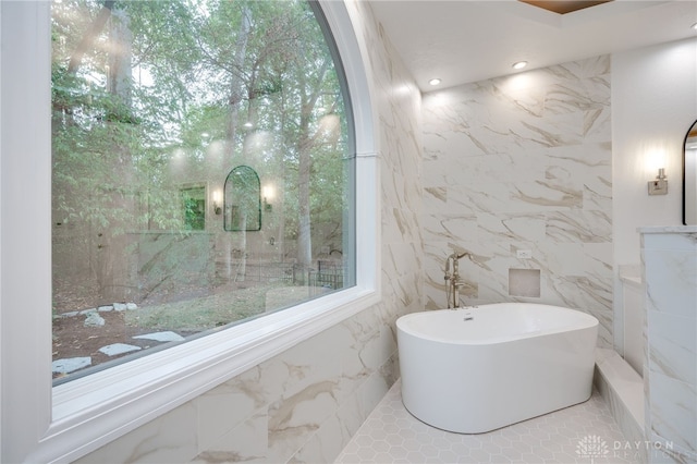 bathroom with a healthy amount of sunlight, tile walls, and a bathtub