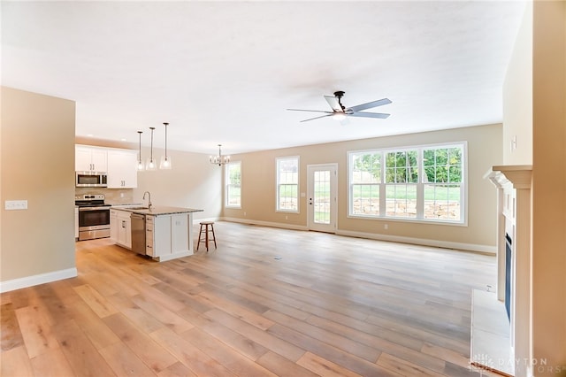 unfurnished living room featuring ceiling fan with notable chandelier, light hardwood / wood-style flooring, plenty of natural light, and sink