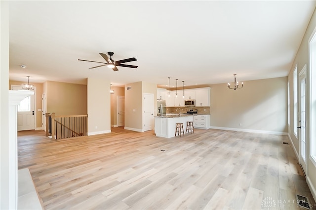 unfurnished living room featuring ceiling fan with notable chandelier, light hardwood / wood-style flooring, a healthy amount of sunlight, and sink