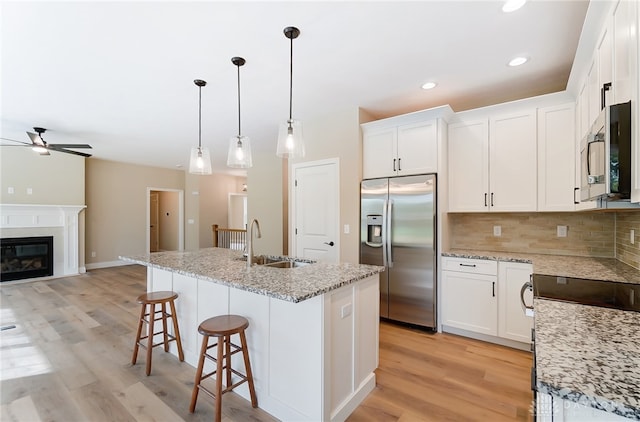 kitchen with light hardwood / wood-style floors, white cabinetry, stainless steel appliances, ceiling fan, and a center island with sink