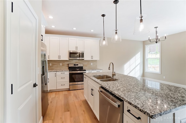 kitchen with an island with sink, hanging light fixtures, sink, white cabinetry, and stainless steel appliances