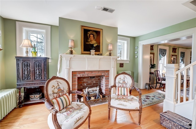 living area with a brick fireplace, light wood-type flooring, and radiator heating unit