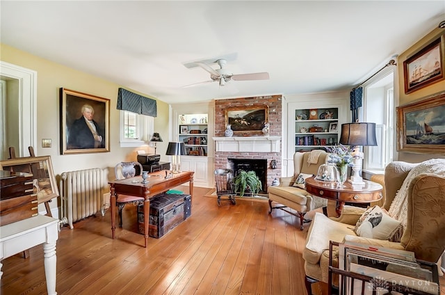 living room featuring a brick fireplace, radiator heating unit, wood-type flooring, ceiling fan, and built in features