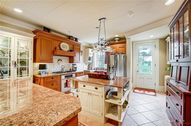 kitchen with appliances with stainless steel finishes, hanging light fixtures, a kitchen island, and light tile patterned floors