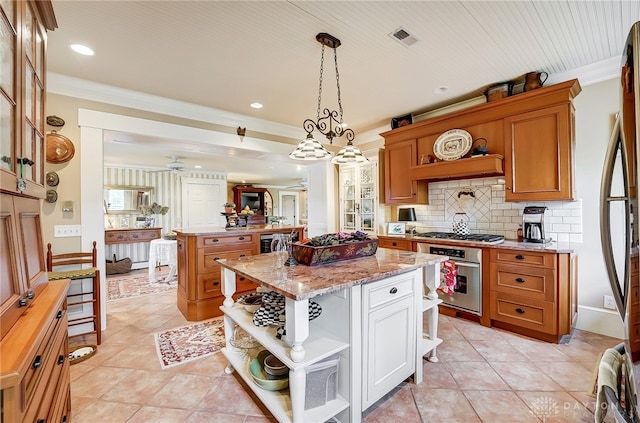 kitchen with light stone counters, ceiling fan, hanging light fixtures, a kitchen island, and appliances with stainless steel finishes