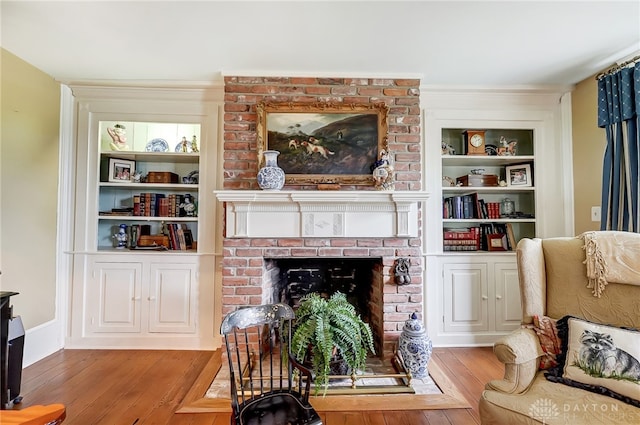 living room with a brick fireplace, light hardwood / wood-style flooring, and built in features