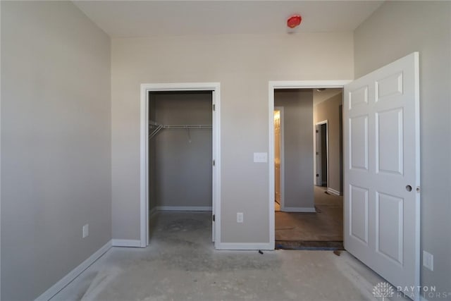 unfurnished bedroom with a spacious closet, concrete flooring, baseboards, and a closet