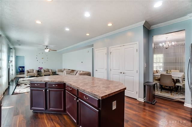 kitchen with crown molding, ceiling fan with notable chandelier, a kitchen island, and dark wood-type flooring