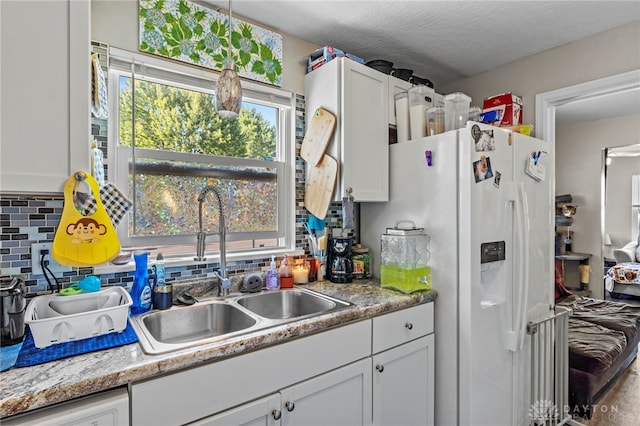 kitchen featuring white cabinets, white fridge with ice dispenser, tasteful backsplash, and sink