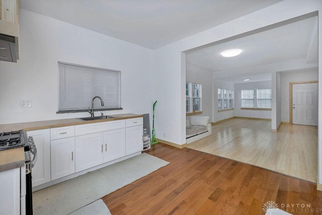 kitchen with stainless steel gas stove, sink, white cabinets, and light wood-type flooring