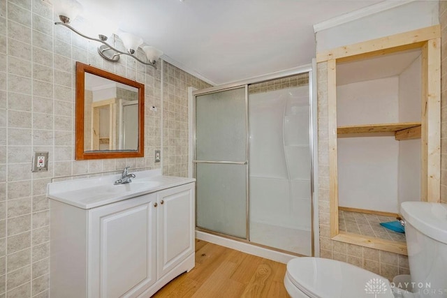 bathroom featuring a shower with shower door, tile walls, hardwood / wood-style flooring, vanity, and toilet