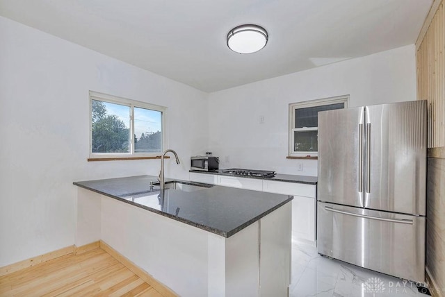 kitchen featuring appliances with stainless steel finishes, white cabinetry, sink, dark stone counters, and kitchen peninsula